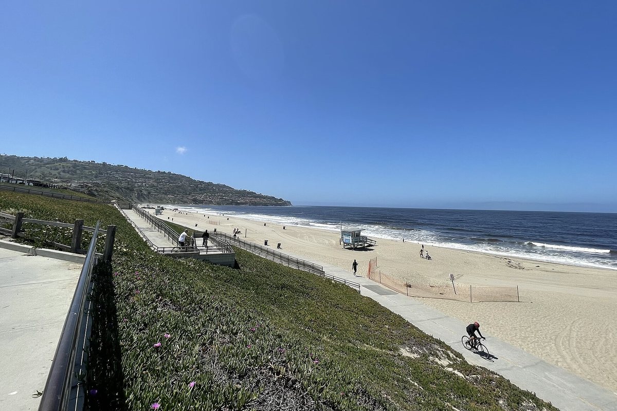 A wide view of Torrance Beach from a bluff-top path, with the bike path along the sand and the Palos Verdes Peninsula in the distance.