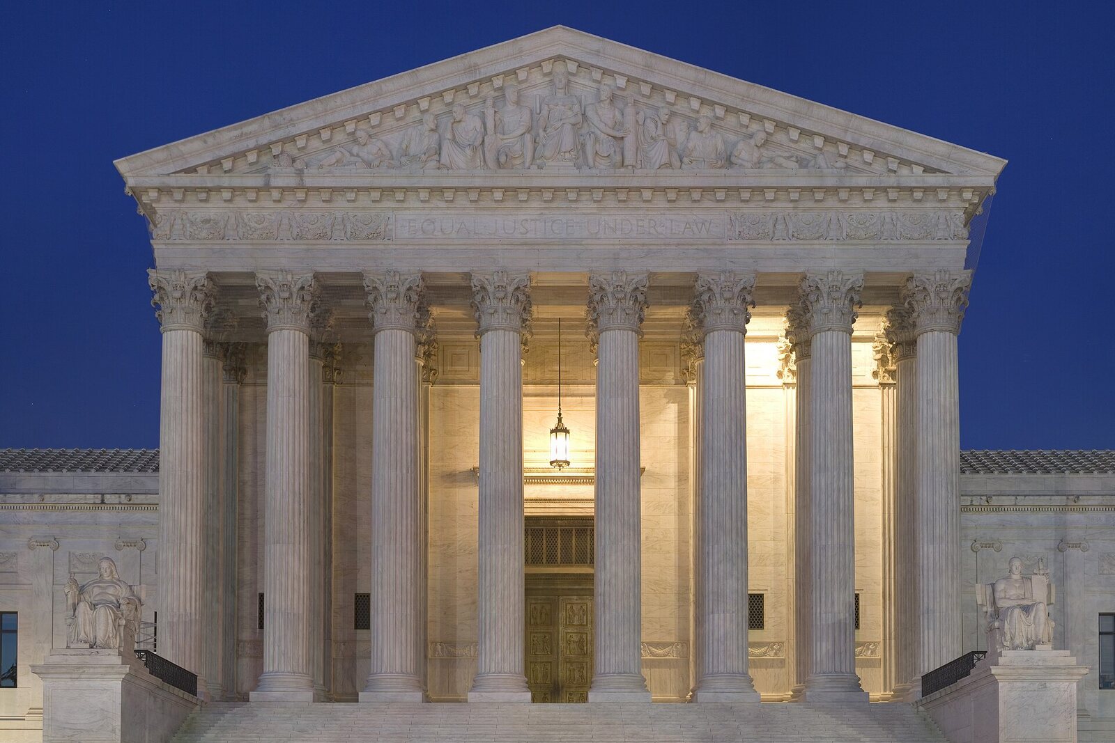 The west front of the U.S. Supreme Court Building at dusk, its eight columns lit from behind against a deep blue sky.