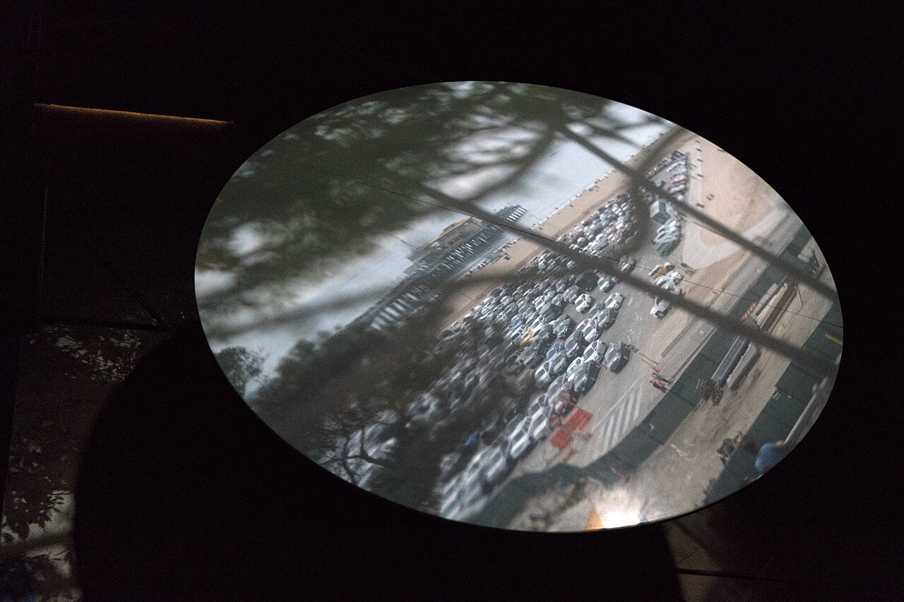 The Santa Monica camera obscura's live image projected onto a round table in a darkened room, showing Ocean Avenue traffic and park trees.