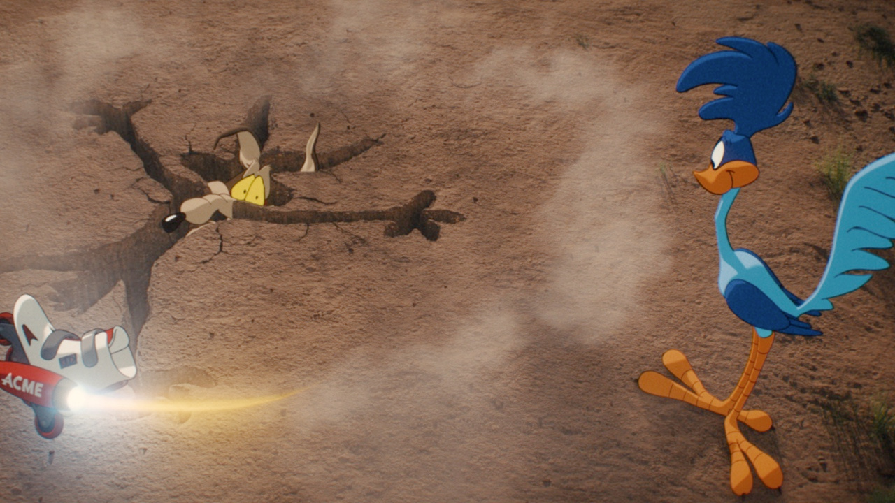 Still from Coyote vs. Acme: Wile E. Coyote face-down in a cracked desert impact crater as an Acme rocket burns nearby and the Road Runner stands over him, unhurt.