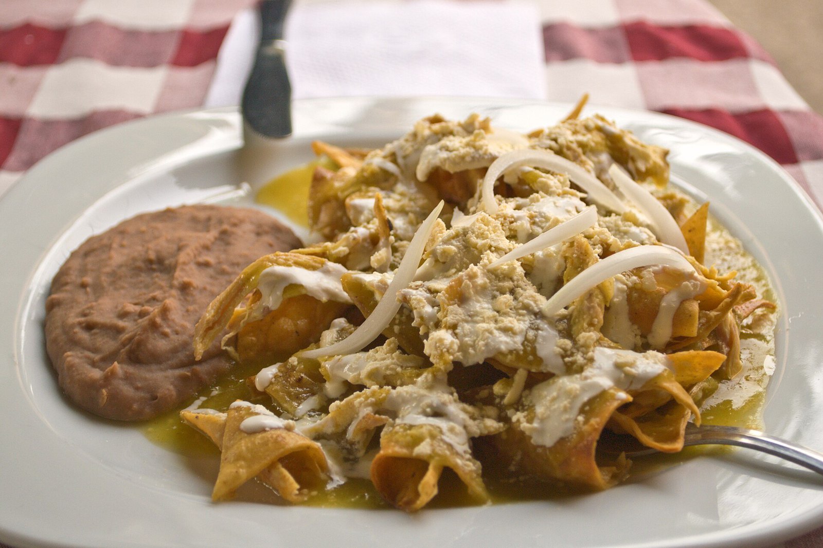 A plate of chilaquiles verdes with refried beans, crema and sliced onion at a Mexico City restaurant, not at Swingers.