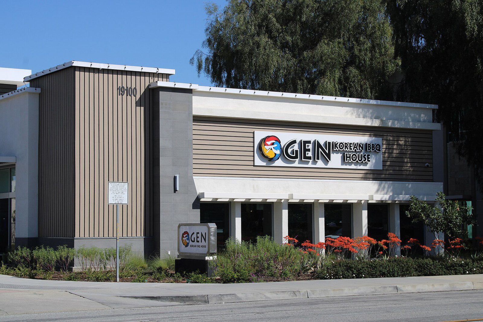 The GEN Korean BBQ House building in Cerritos, with its sign over the entrance and red flowers along the front.