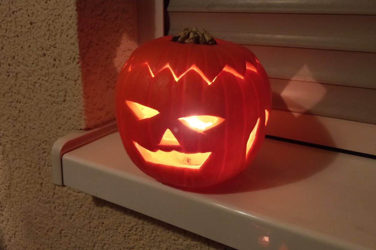 A carved jack-o'-lantern lit from the inside by a candle, sitting on a windowsill at night.
