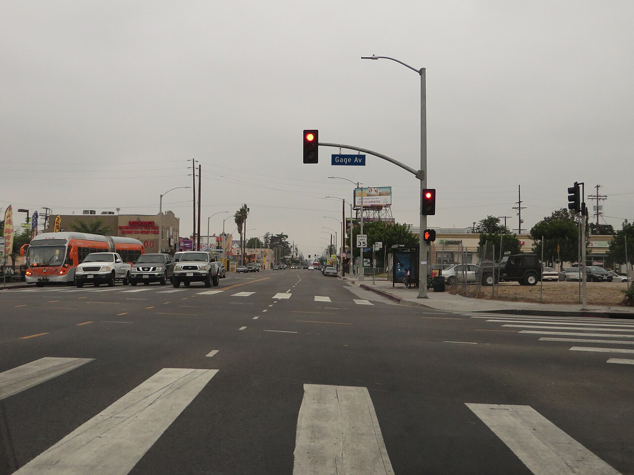 Vermont Avenue at Gage Avenue in South Los Angeles under a gray marine layer, with cars parked along the curb and a Metro bus at the intersection