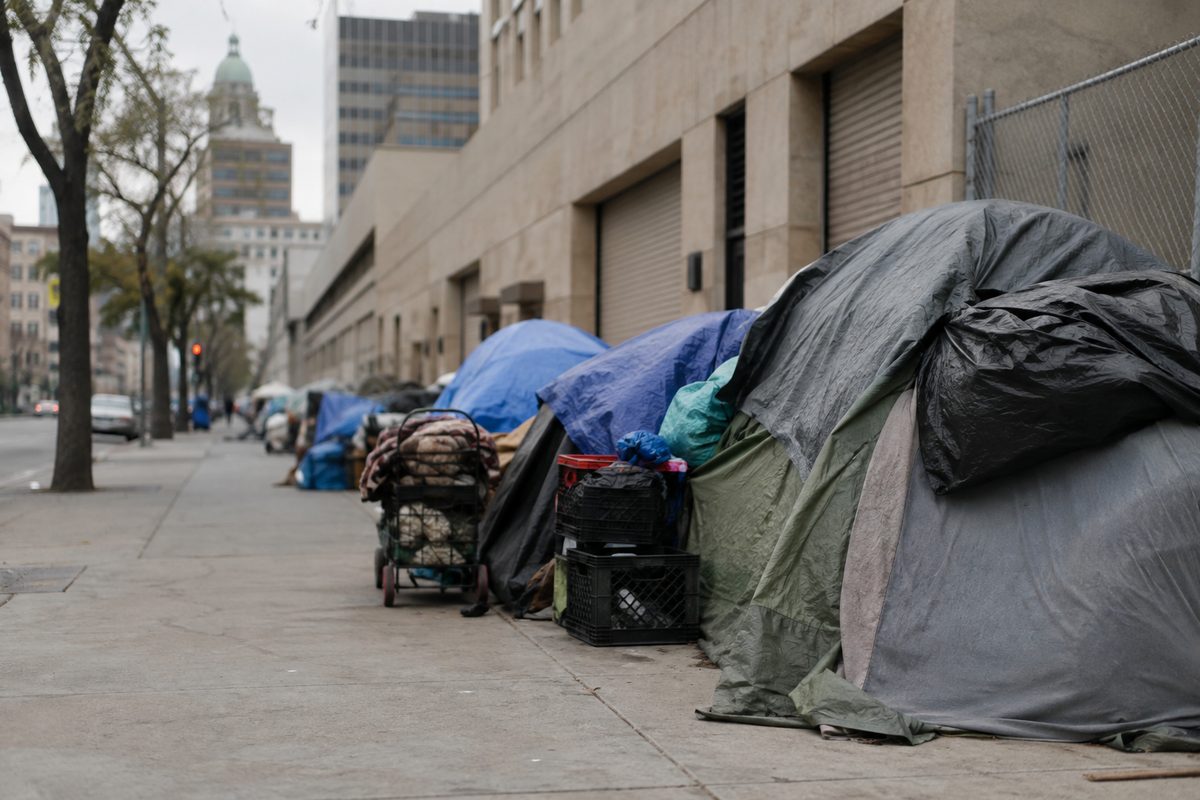 A row of tents and belongings along a downtown Los Angeles sidewalk beside a wide empty street, LAUSD-adjacent urban homelessness scene