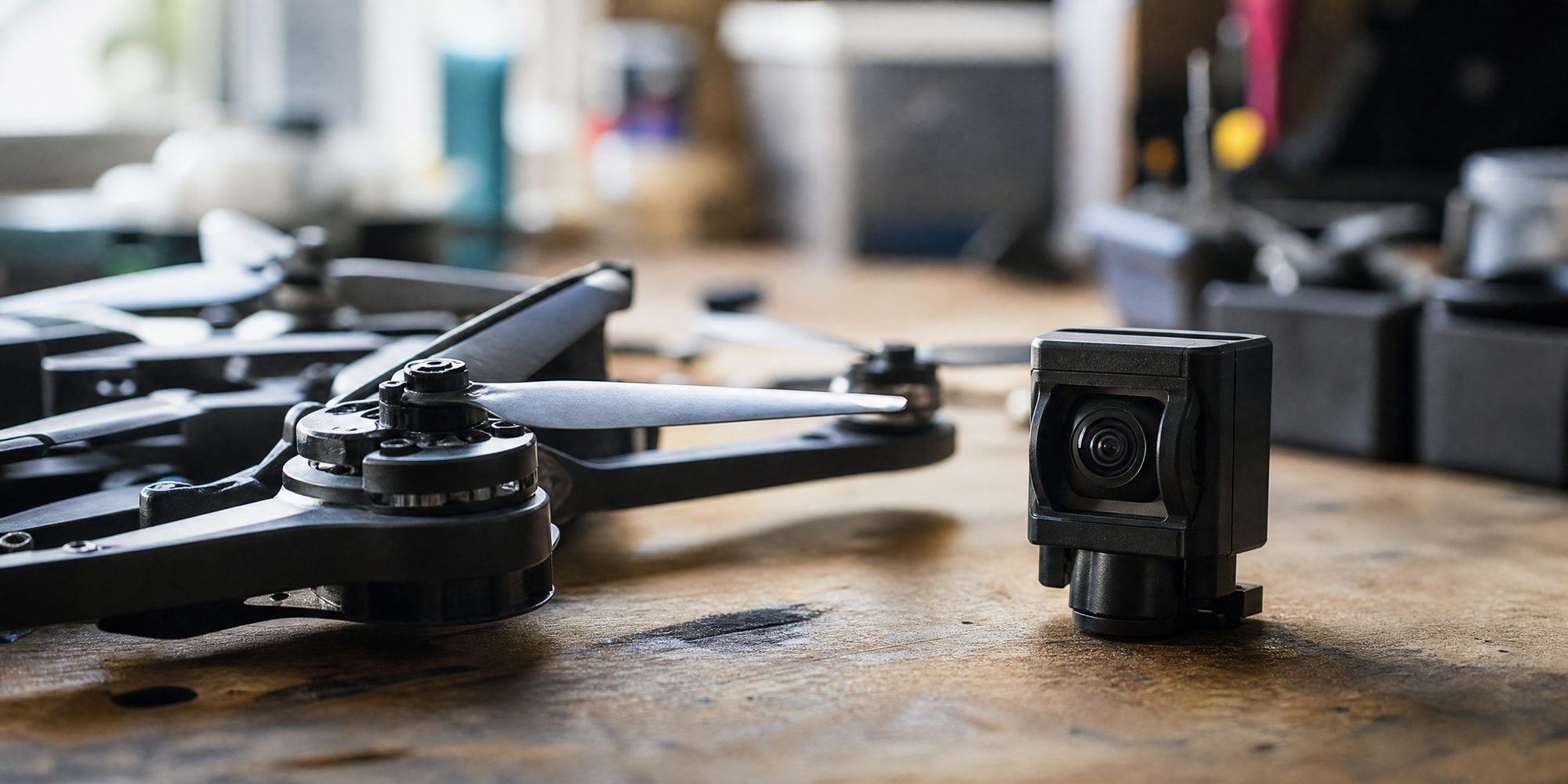 Close-up of small drone propeller arms beside a palm-sized camera module on a workbench, illustrating the FCC drone ban affecting the HoverAir Versa camera-drone.