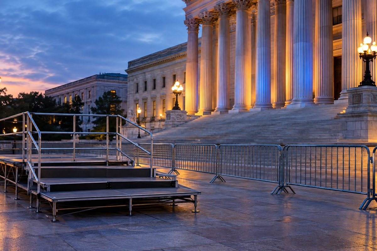 An empty press riser behind a metal barricade outside a neoclassical government building at dusk.