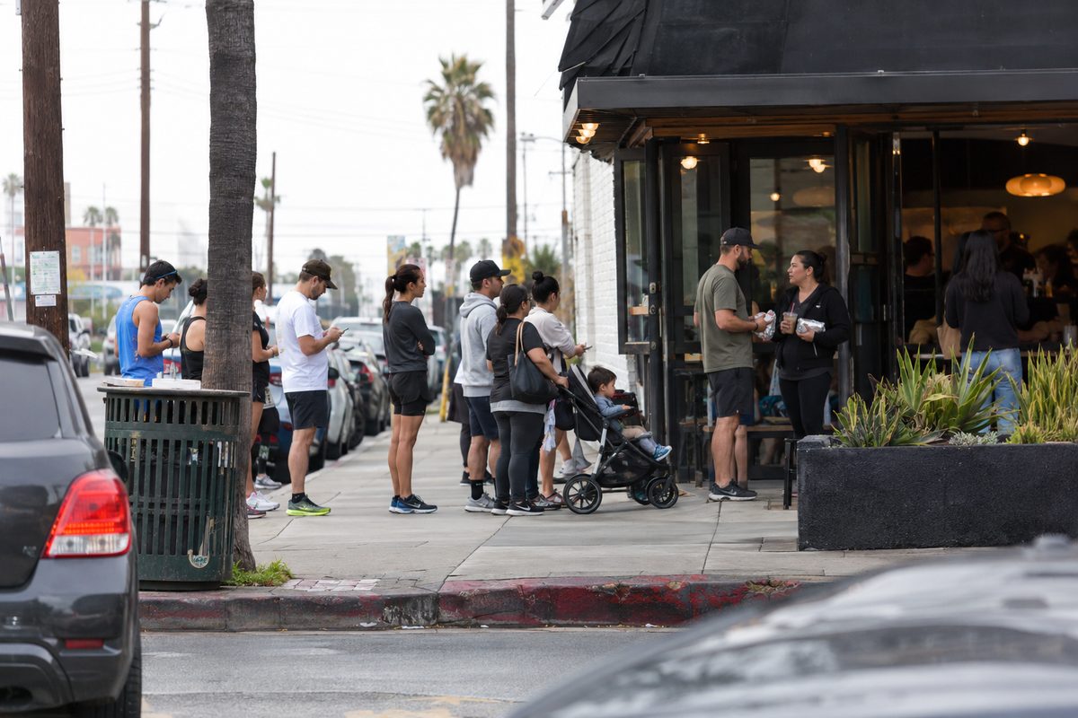 People wait in line outside a small cafe on East 4th Street in Long Beach on an overcast morning, some holding foil-wrapped burritos.