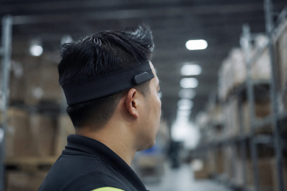 An unidentified worker in a warehouse wears a plain sensor headband of the kind used in workplace brain-data monitoring.