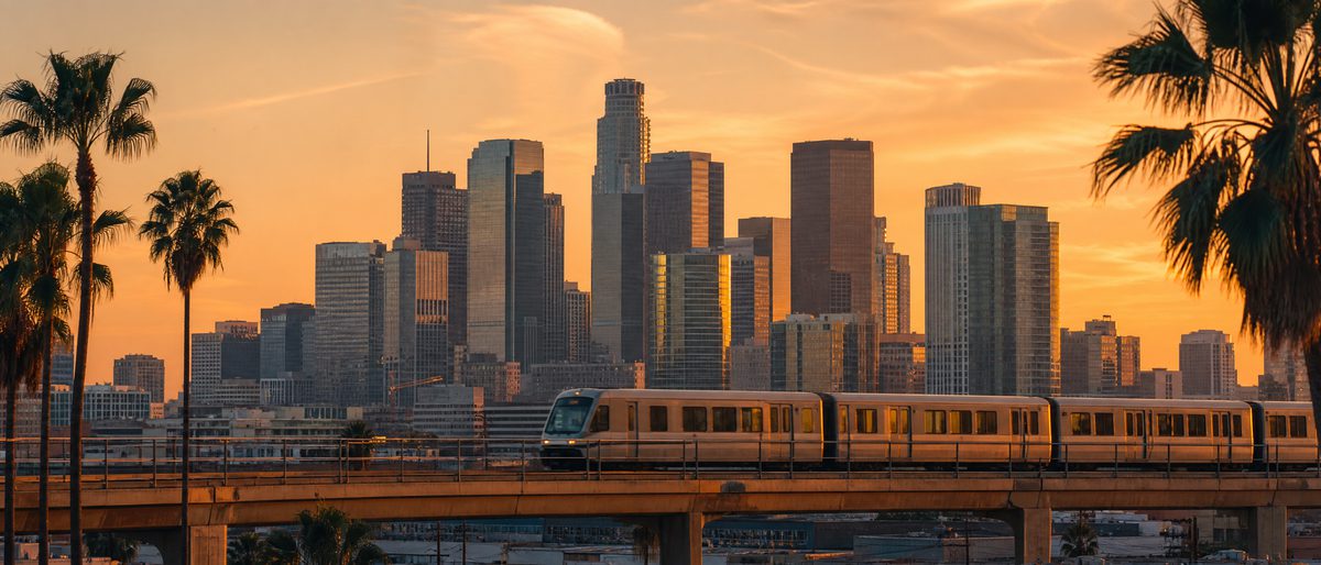 An elevated Metro train before the downtown skyline at sunset