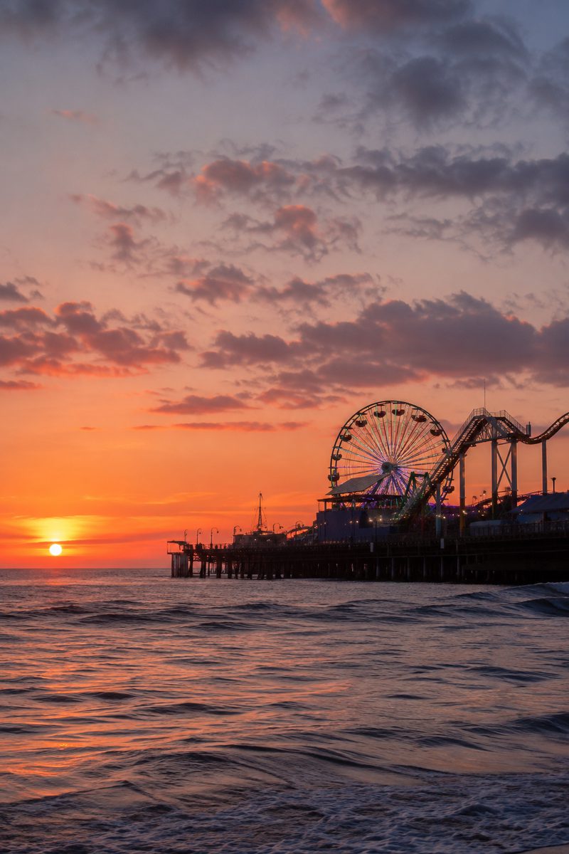 A lit ferris wheel on an oceanfront pier at sunset