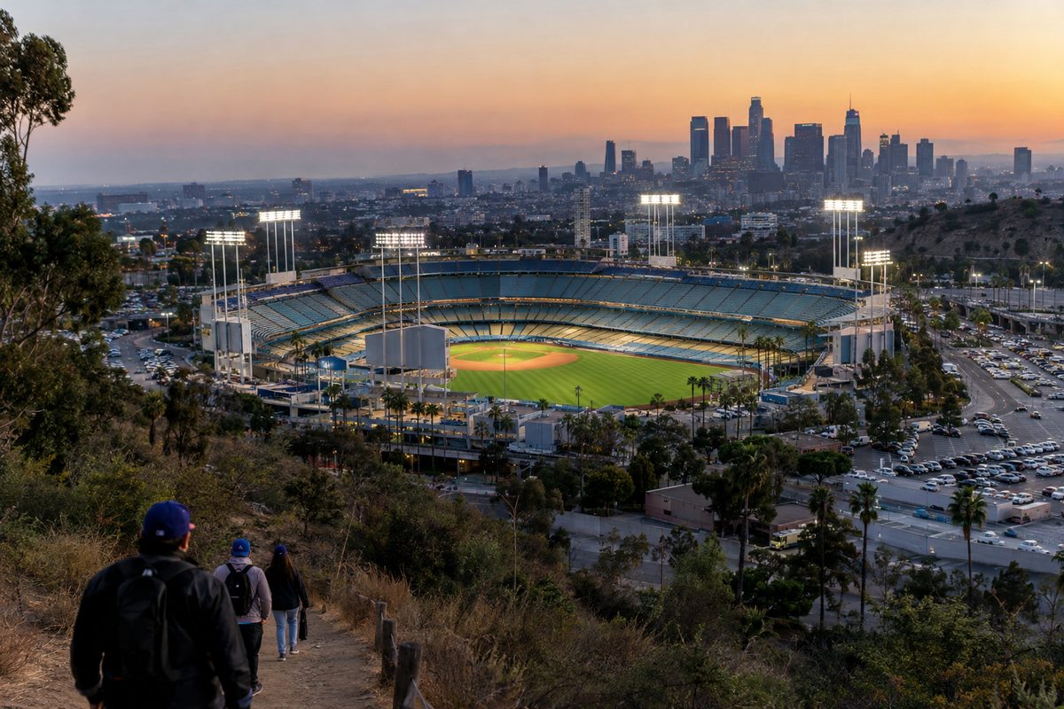Dodger Stadium seen from a hillside in Elysian Park at dusk, light towers on over an empty field.