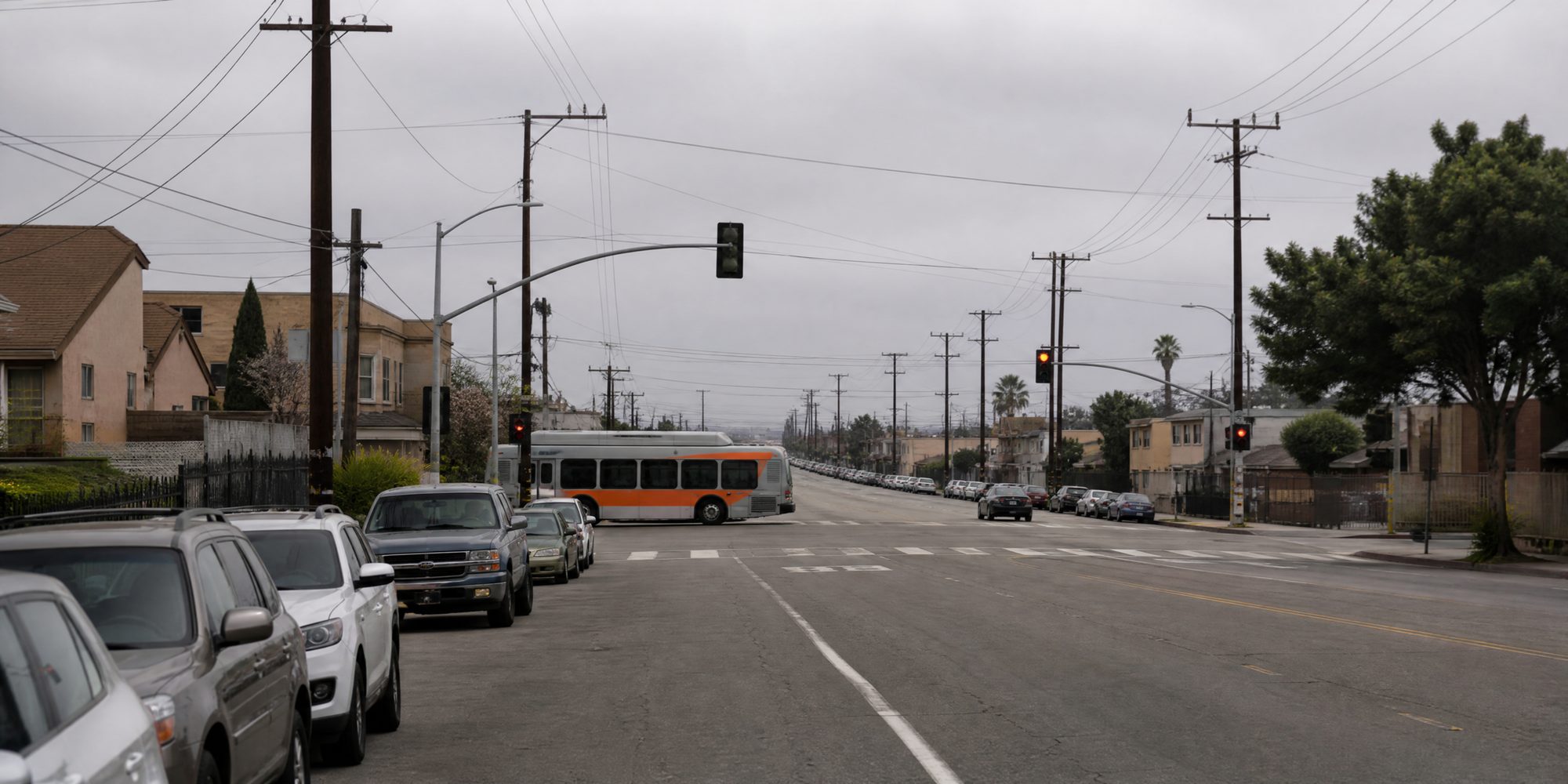 Vermont Avenue at Gage Avenue in South Los Angeles under a gray marine layer, with cars parked along the curb and a Metro bus at the intersection