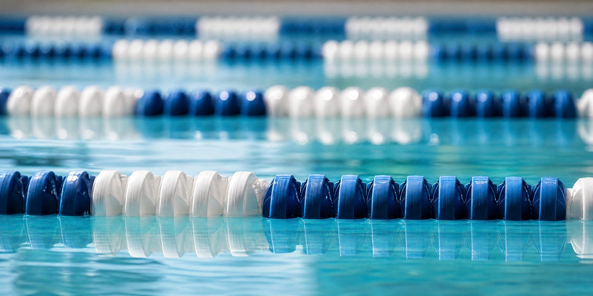Photo illustration: extreme macro of blue-and-white lane ropes floating on still indoor pool water, hard overhead light, no swimmers, no signage, no venue identifiers