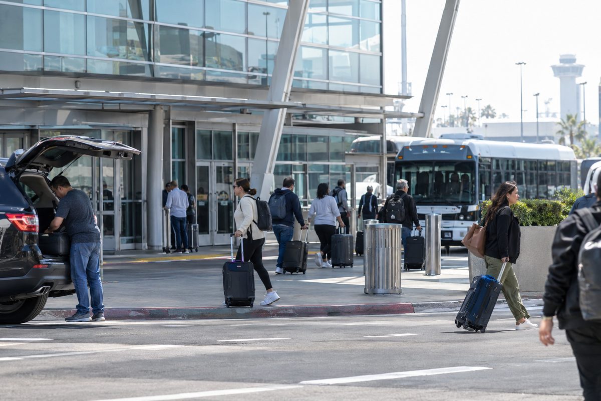Travelers pull suitcases along the upper-level departures curb outside the Tom Bradley International Terminal at Los Angeles International Airport at midday.