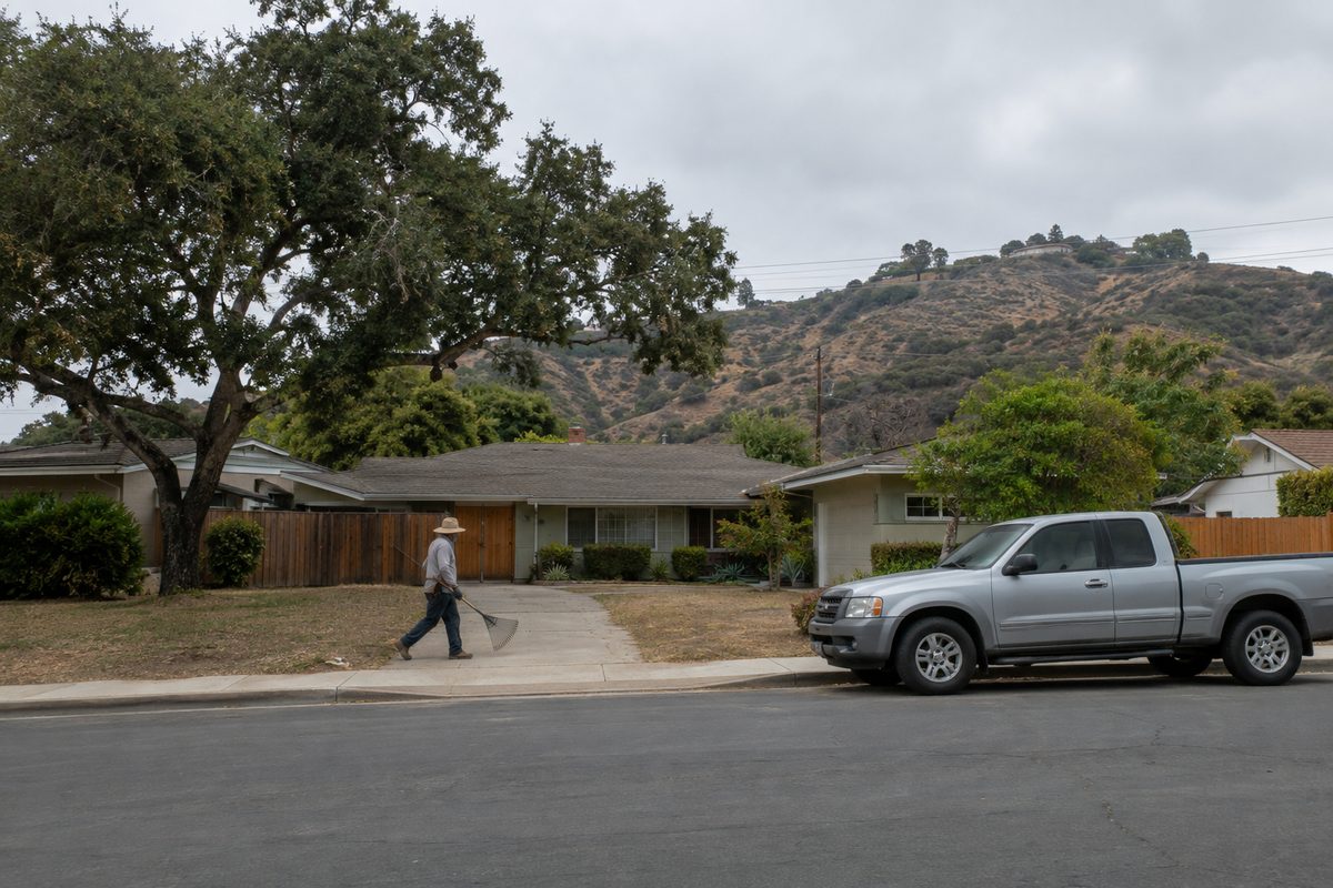 A quiet residential street in Westlake Village under an overcast sky, with backyard fences, oak trees and chaparral-covered hills behind the houses.