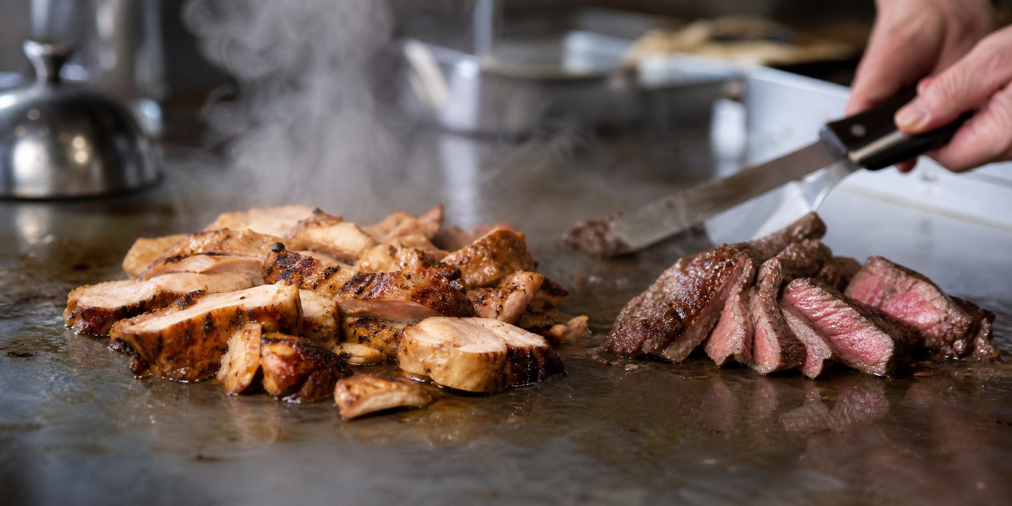 Close-up of sliced grilled chicken and steak resting on a steel kitchen surface, steam rising, hands working at the edge of the frame.
