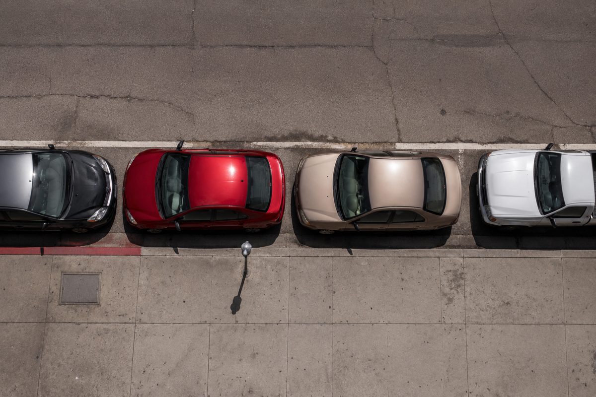 Overhead view of cars parked along a curb on a residential Los Angeles street at midday, with a painted red zone and hard shadows.