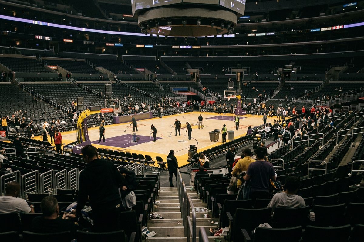 Photo illustration: Last night in Los Angeles sports: a Los Angeles arena's basketball court after the final buzzer at night, the bowl's lights half down and a crew sweeping the hardwood, seen from the upper seats.