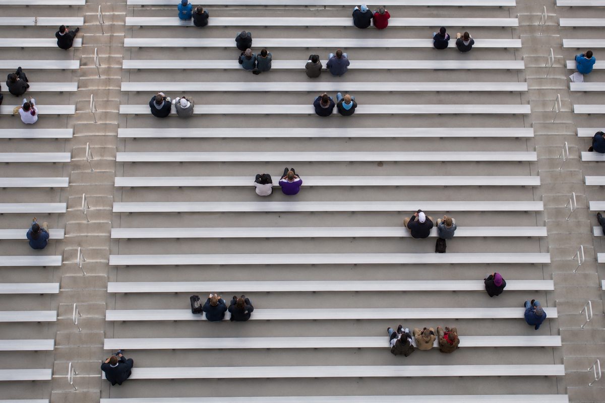 Overhead view of curving concrete-and-aluminum stadium bleacher rows, mostly empty, in flat gray morning light.