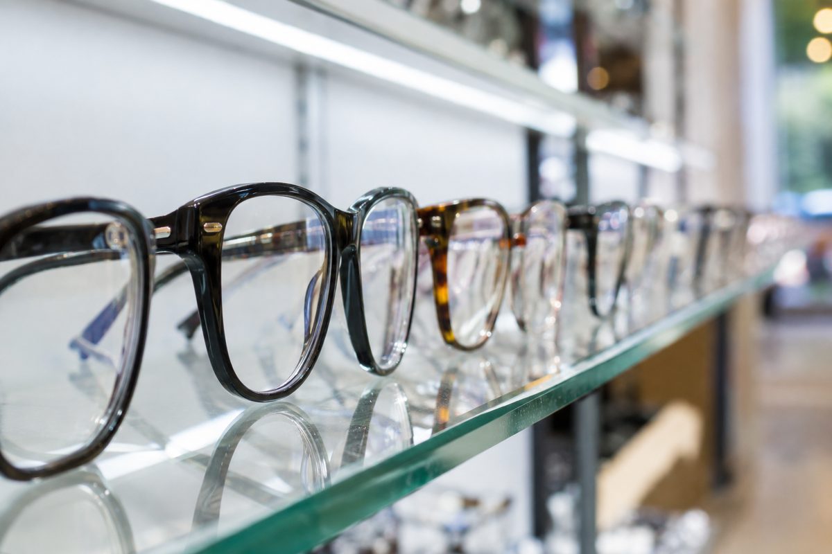 Rows of unbranded eyeglass frames lined up on a lit retail display shelf, shot from the side.