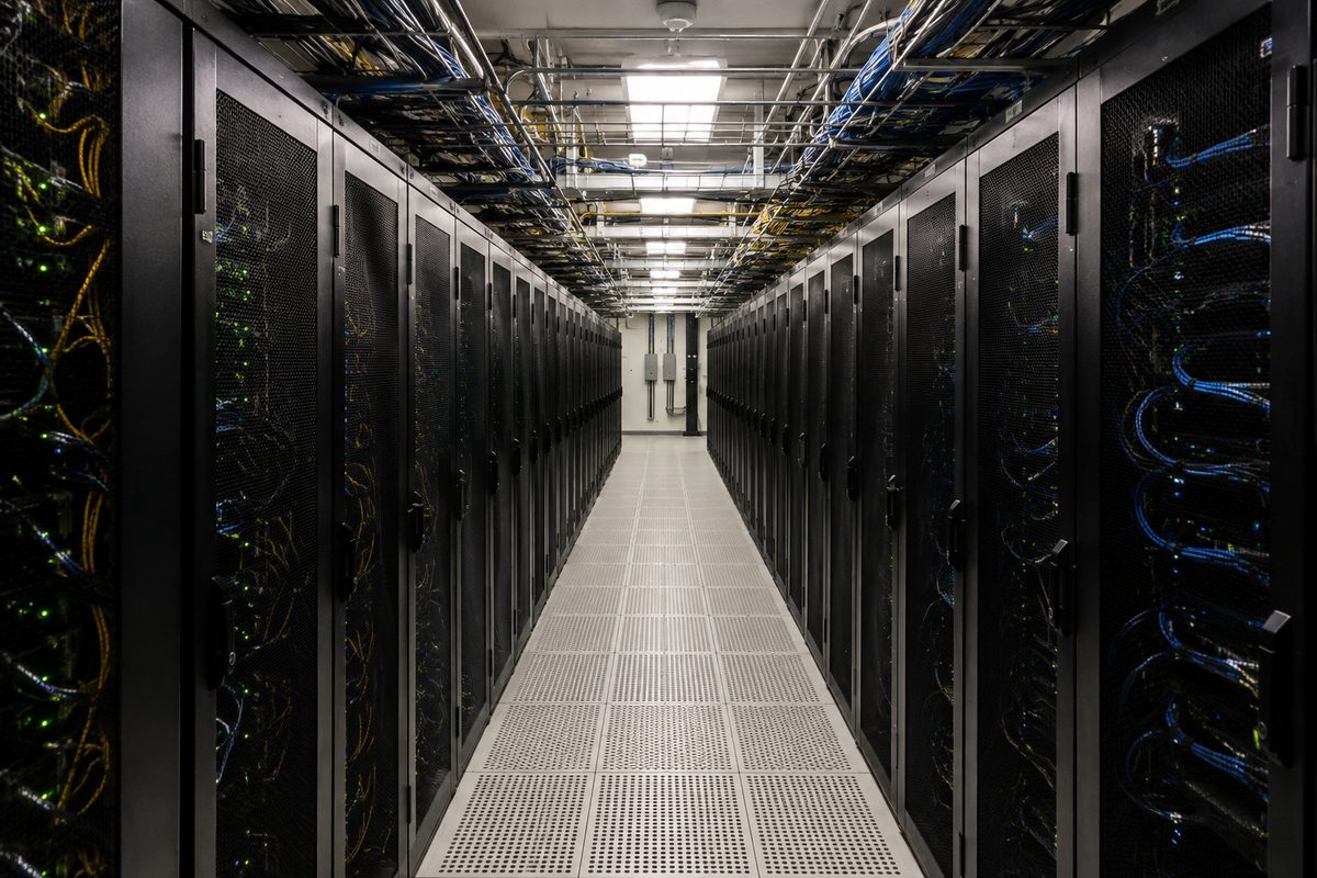 A symmetrical frontal view down a data center aisle: rows of unbranded server racks with blinking indicator lights, bundled cabling in overhead trays, lit by flat fluorescent ceiling panels.