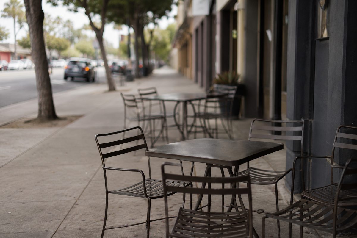 Empty outdoor dining tables and chairs on a sidewalk in a Southern California commercial strip, no people or business names visible