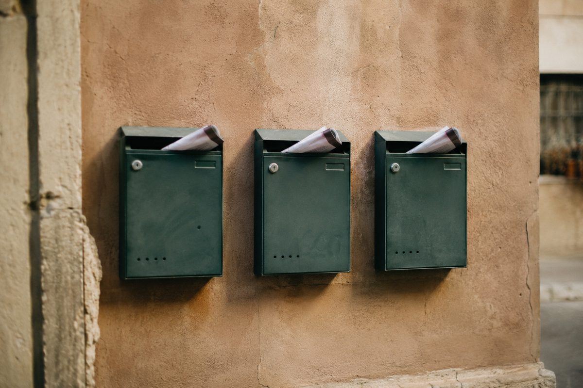 Photo illustration: three apartment mailboxes in a row on a sun-faded stucco wall, a folded notice tucked into each one, flat editorial illustration, muted brand palette, no text, no people