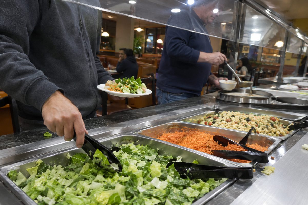 Diners use tongs to fill plates at a long self-serve salad bar under a sneeze guard, like the ones Souplantation was known for in California.