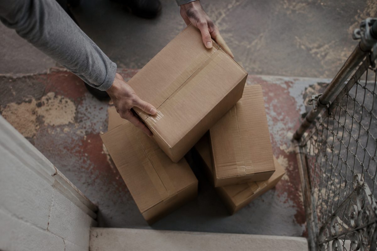 Overhead view of plain brown cardboard parcels stacked on a stucco apartment stoop in soft morning light, with no visible logos or labels.