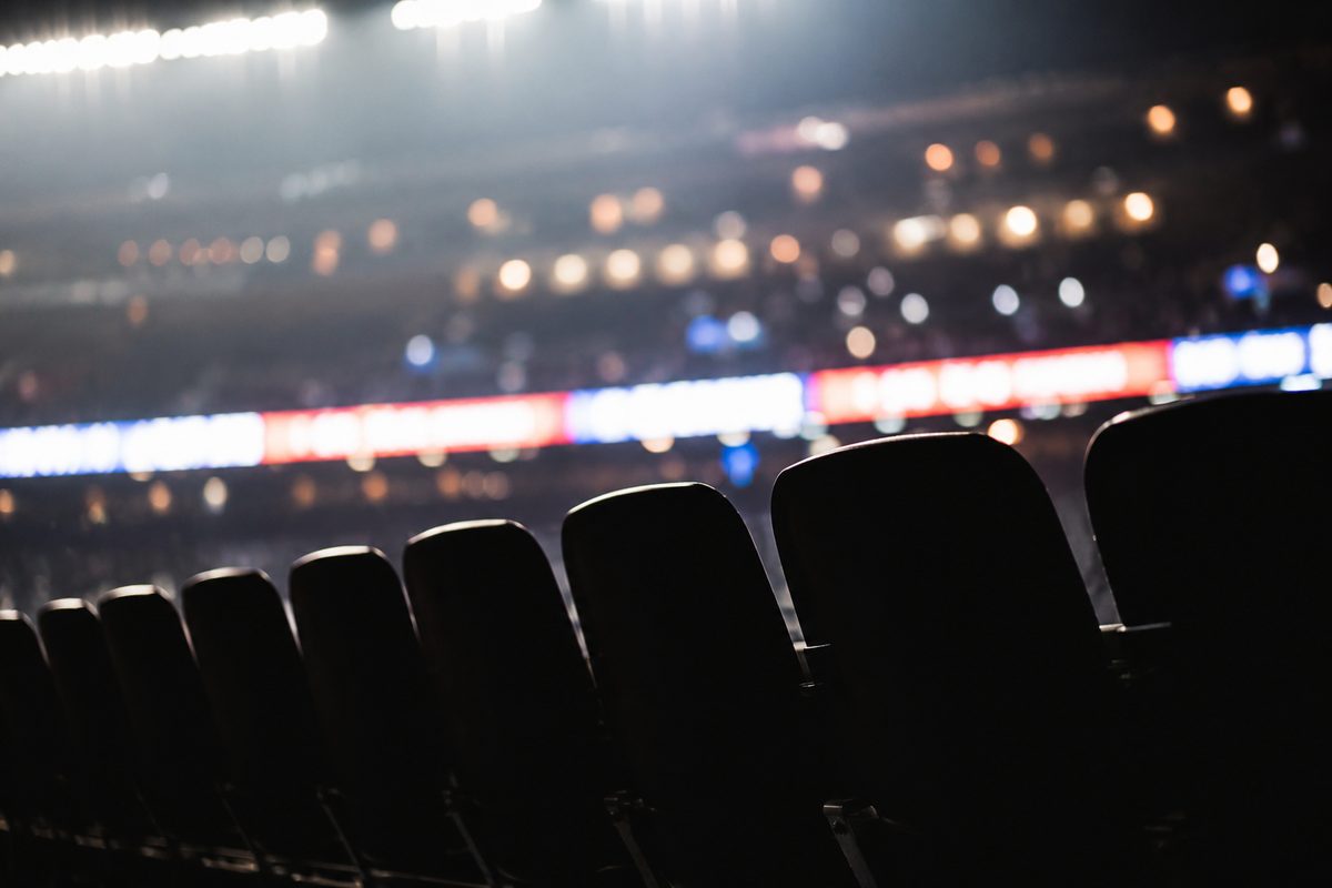 Silhouetted empty stadium seats at night with the blurred glow of an LED ribbon board, its text unreadable.