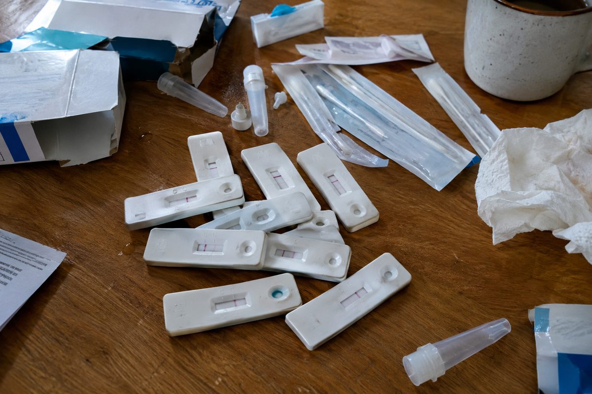 Photo illustration of used rapid flu, COVID and RSV tests piled on a kitchen table, each test window showing a single line.