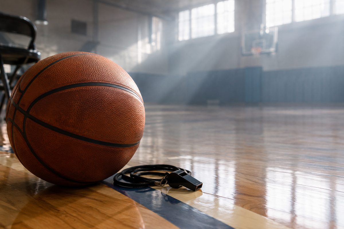 Extreme close-up of a basketball resting on a painted court sideline beside a whistle lanyard in soft morning haze.