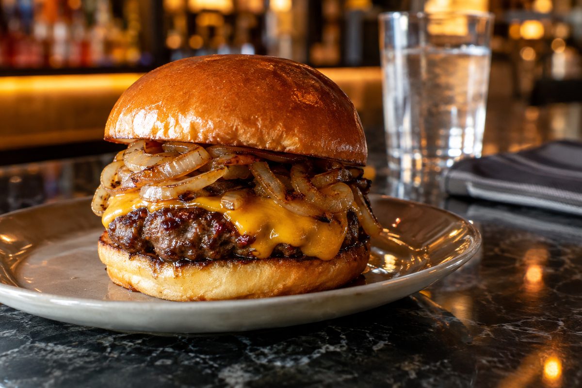 A burger and fries on a plate at a dark bar counter, lit from behind.