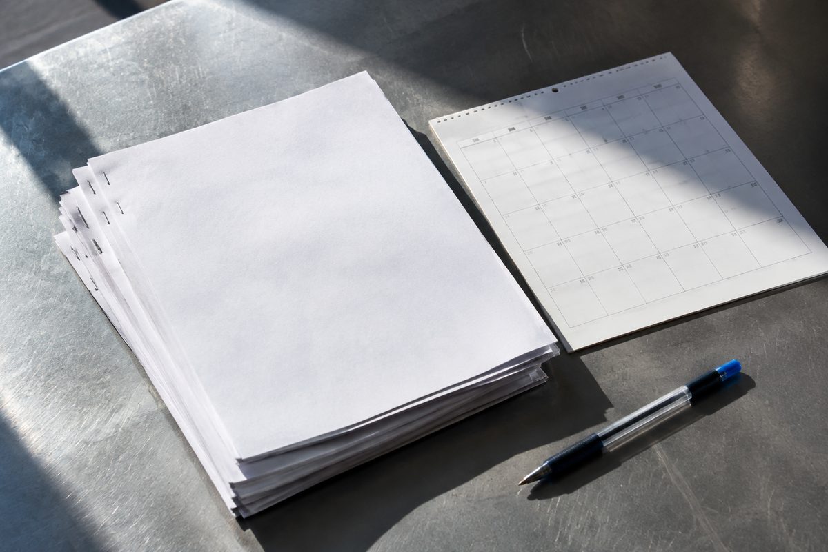 Overhead view of stapled legal documents and a wall calendar on a metal table in hard midday light.