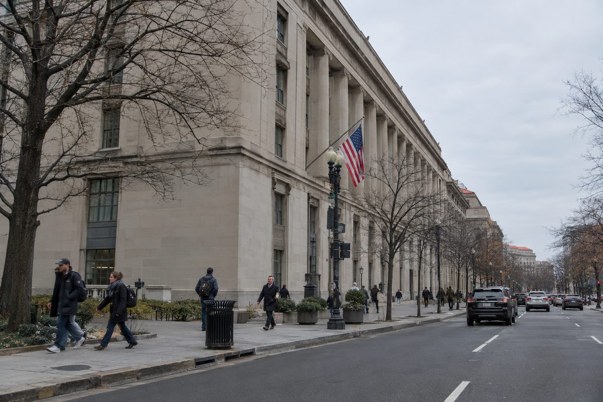 The Justice Department headquarters building in Washington on an overcast morning, with pedestrians walking past along Pennsylvania Avenue.