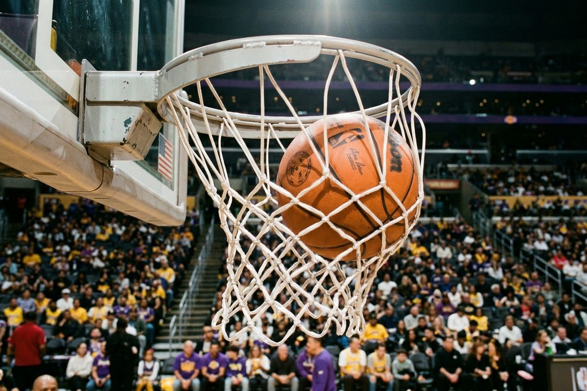 A basketball drops through the net under the arena lights at Crypto.com Arena as fans in purple and gold fill the lower bowl before a Lakers game against the Warriors.