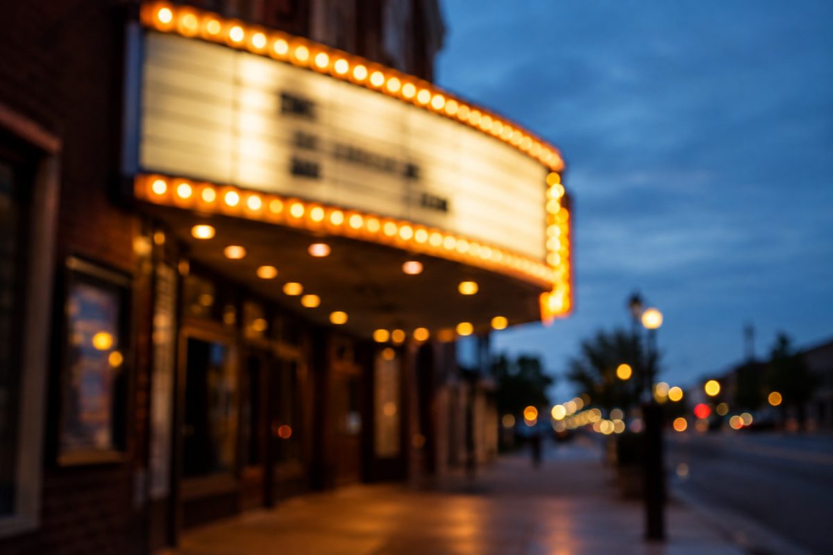 Shallow-focus photograph of a cinema marquee's letter track glowing at dusk, the type out of focus and unreadable.