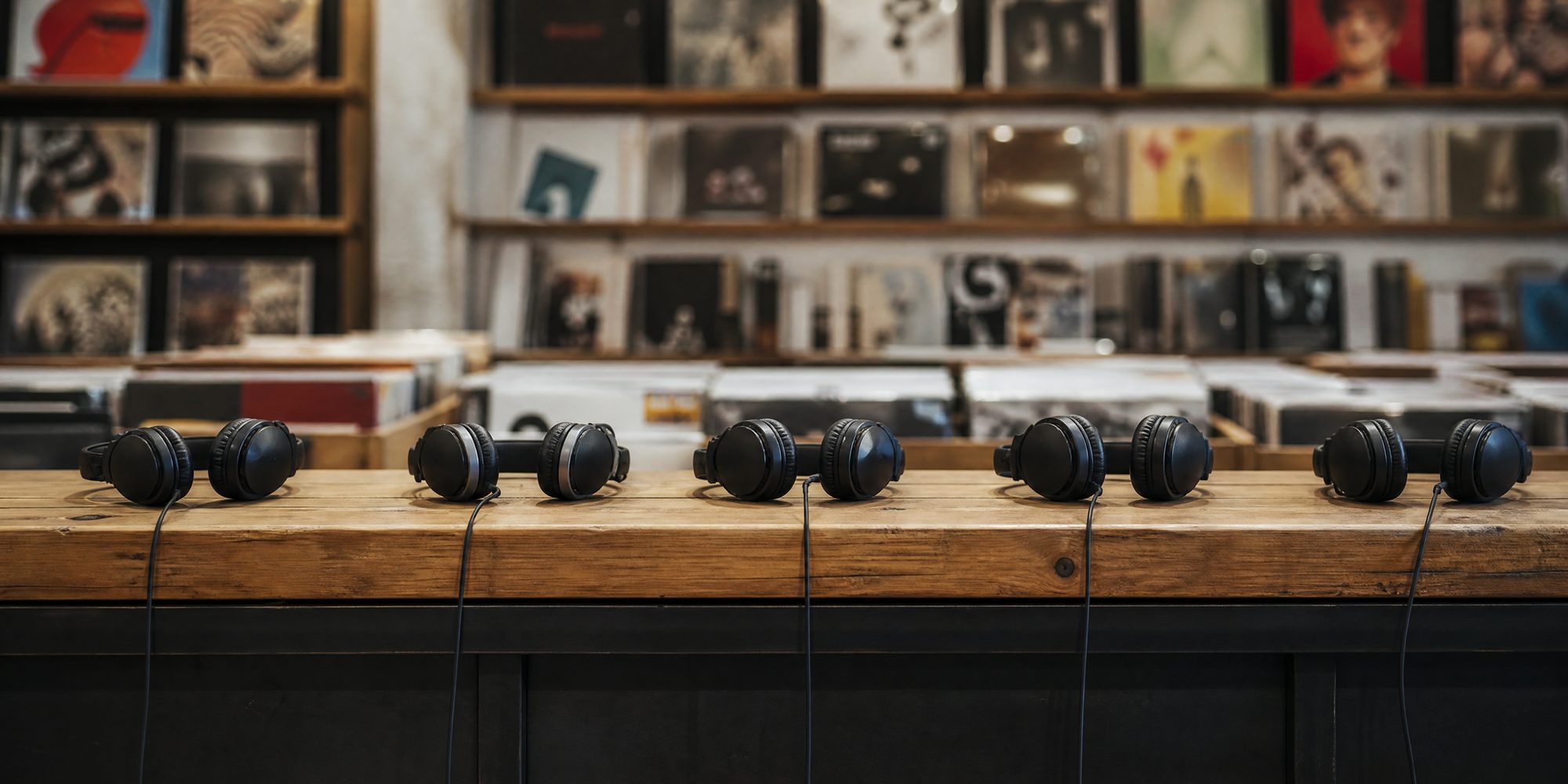A row of headphones resting on a wooden counter at an anonymous record-shop listening station, seen straight on.