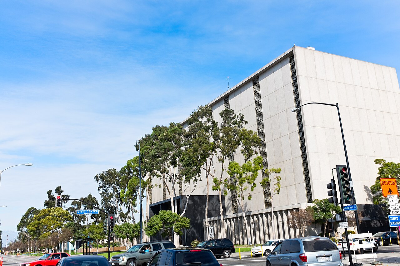 The Los Angeles County Superior Court building in Norwalk, a windowless concrete block set behind eucalyptus trees, with a blue JURY PARKING sign at the Norwalk Boulevard corner
