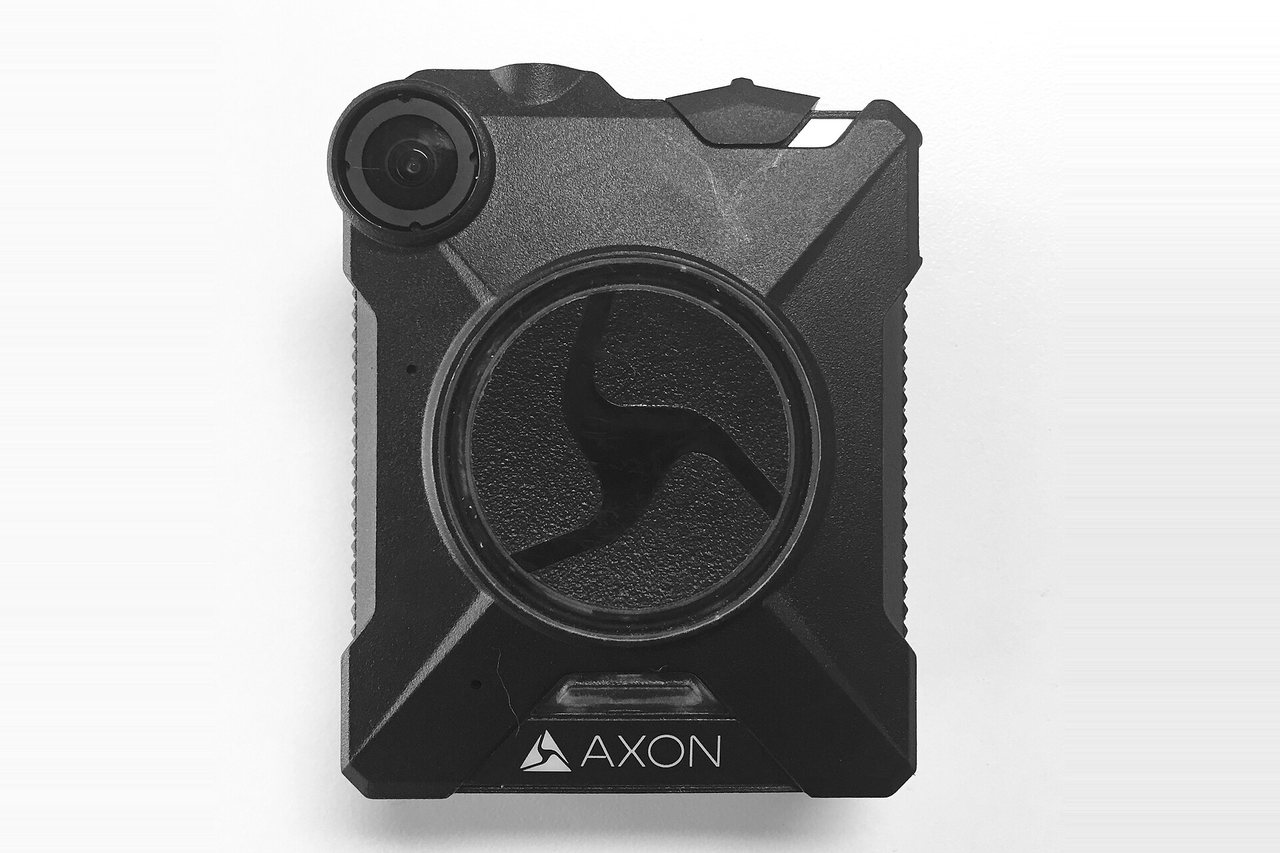 An Axon Body 2 body-worn camera photographed against a plain white background, its lens at the upper left and the round record control at the center of the housing.