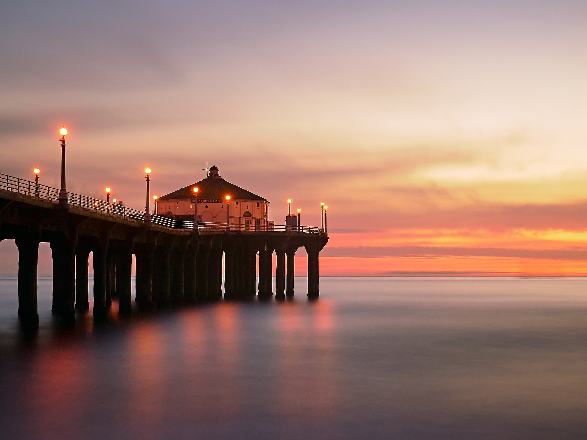 The Manhattan Beach Pier at sunset, its lamps lit and the octagonal Roundhouse standing at the far end