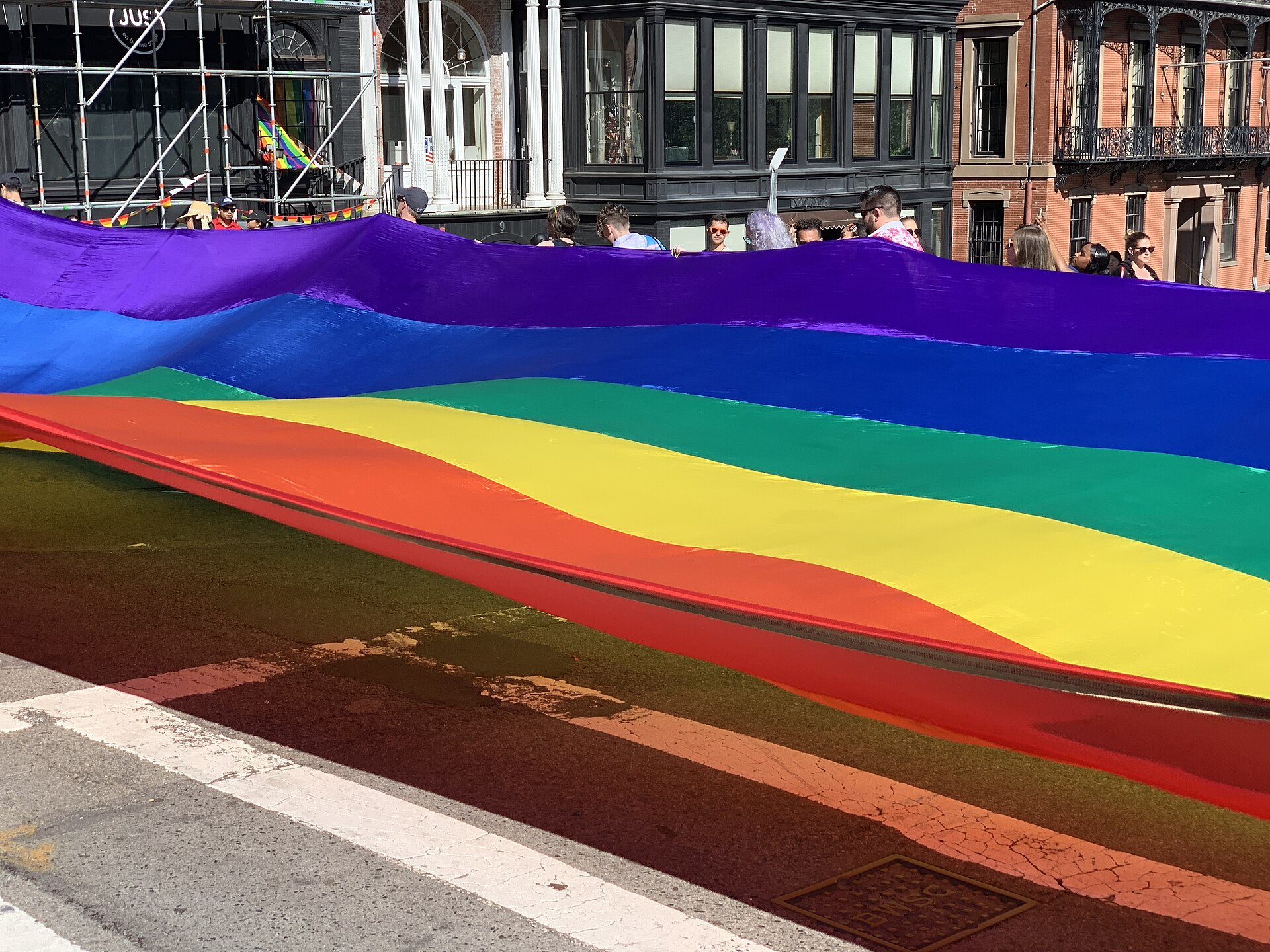A parade-sized rainbow flag carried down a street