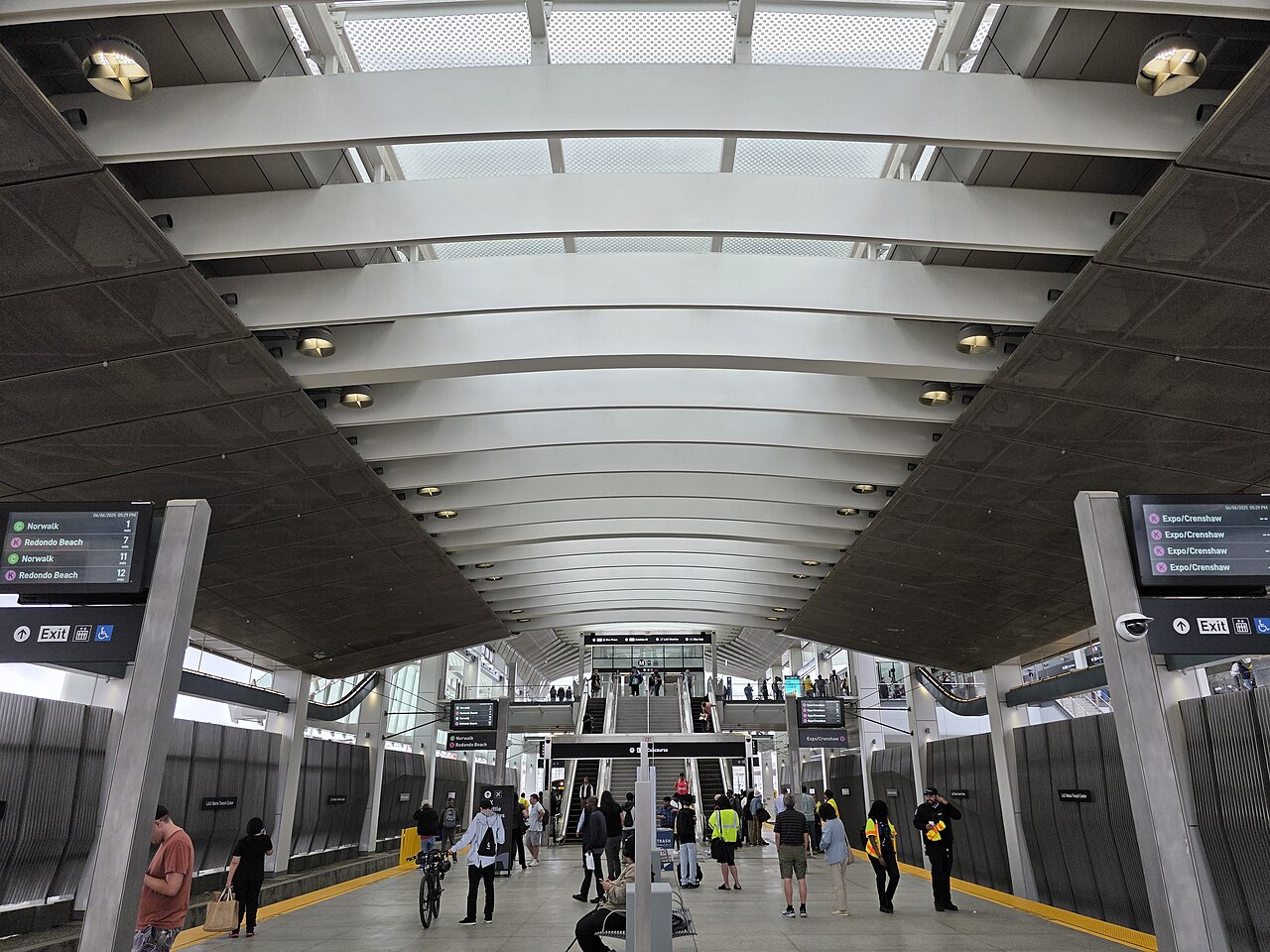 Passengers on the platform at the LAX/Metro Transit Center, with arrival boards for the C and K lines overhead