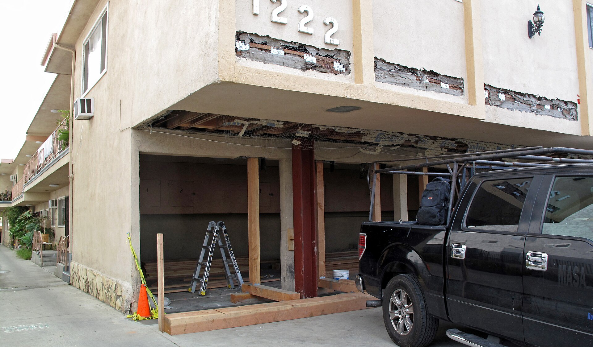 A two-story Los Angeles apartment building with its ground-floor parking opened up for a seismic retrofit, a steel frame in place and stucco cut back to the framing