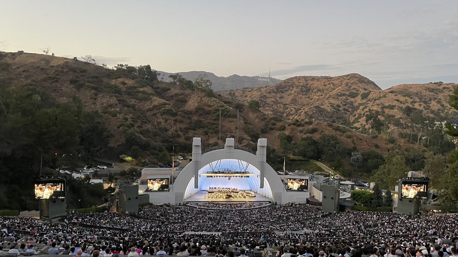 A capacity crowd fills the Hollywood Bowl amphitheater at dusk during an outdoor concert